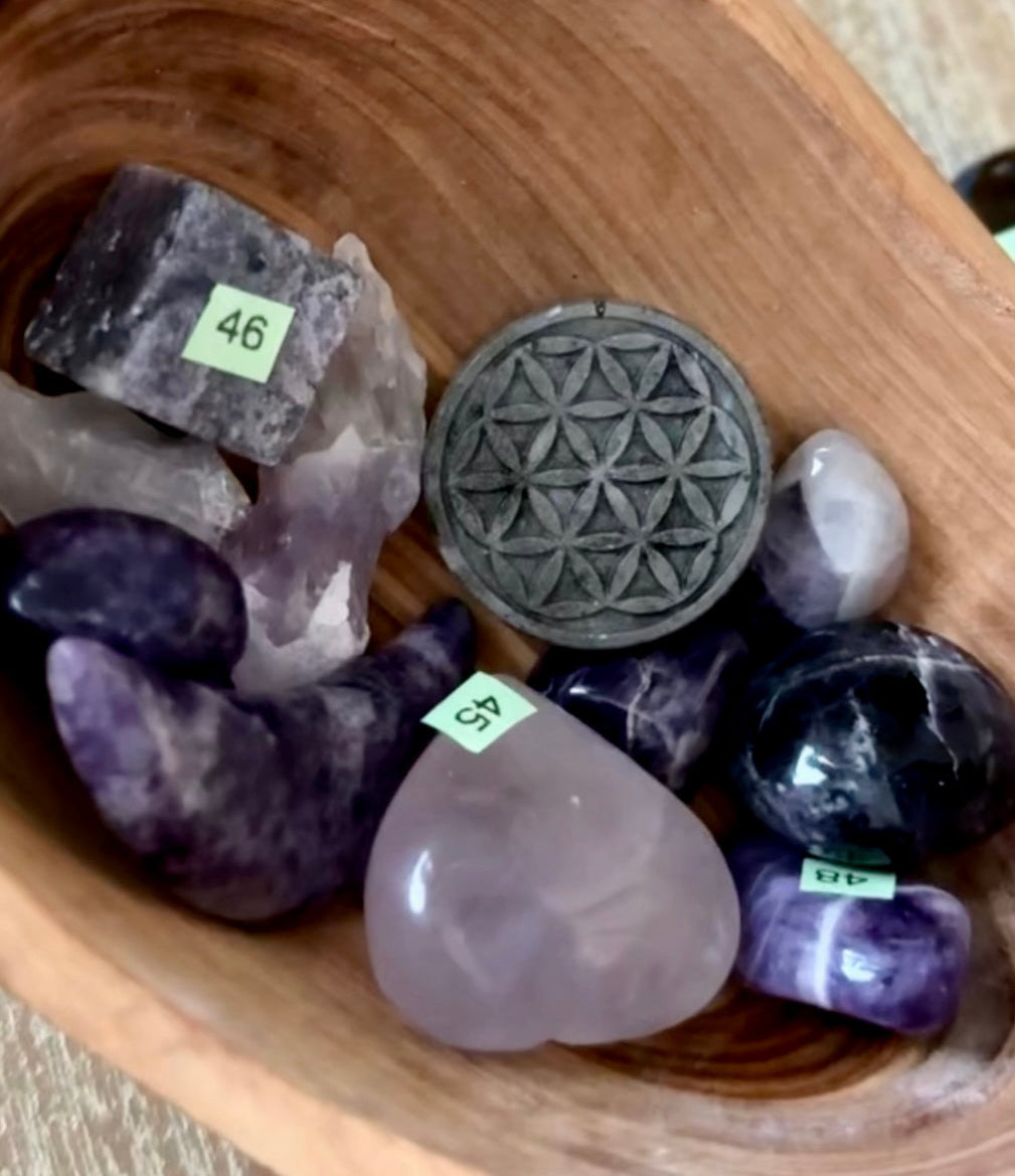 Collection of crystals and a flower of life symbol in a wooden bowl.